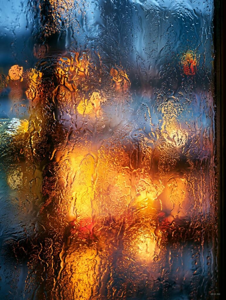 Voda na staklu sa toplim svjetlima grada u pozadini